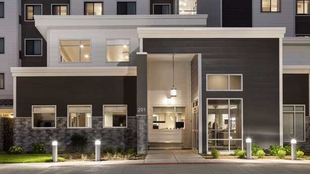 Un immeuble résidentiel moderne à plusieurs étages, doté d’une entrée bien éclairée, de grandes fenêtres et d’une façade en pierre.