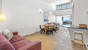 Ein geräumiger Wohnbereich mit einem runden Holztisch, einem roten Sofa und einer Küchenzeile mit Theke.
