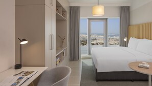 A modern hotel room with a large bed, a desk with a chair, a small table, and a view of the city through the window. - Staybridge Suites Dubai Financial Centre by IHG (Dubai)