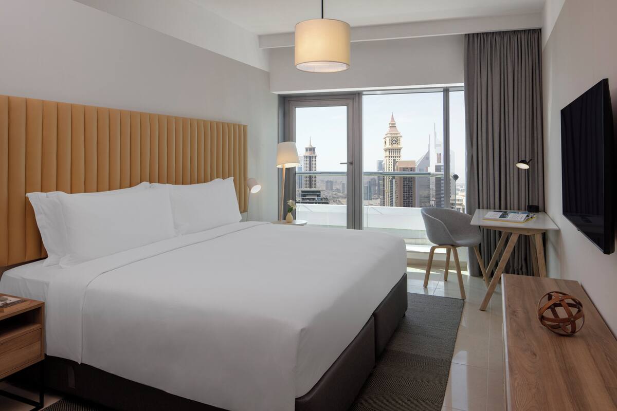 Une chambre d’hôtel moderne dotée d’un grand lit, d’un bureau et offrant une vue sur le paysage urbain.