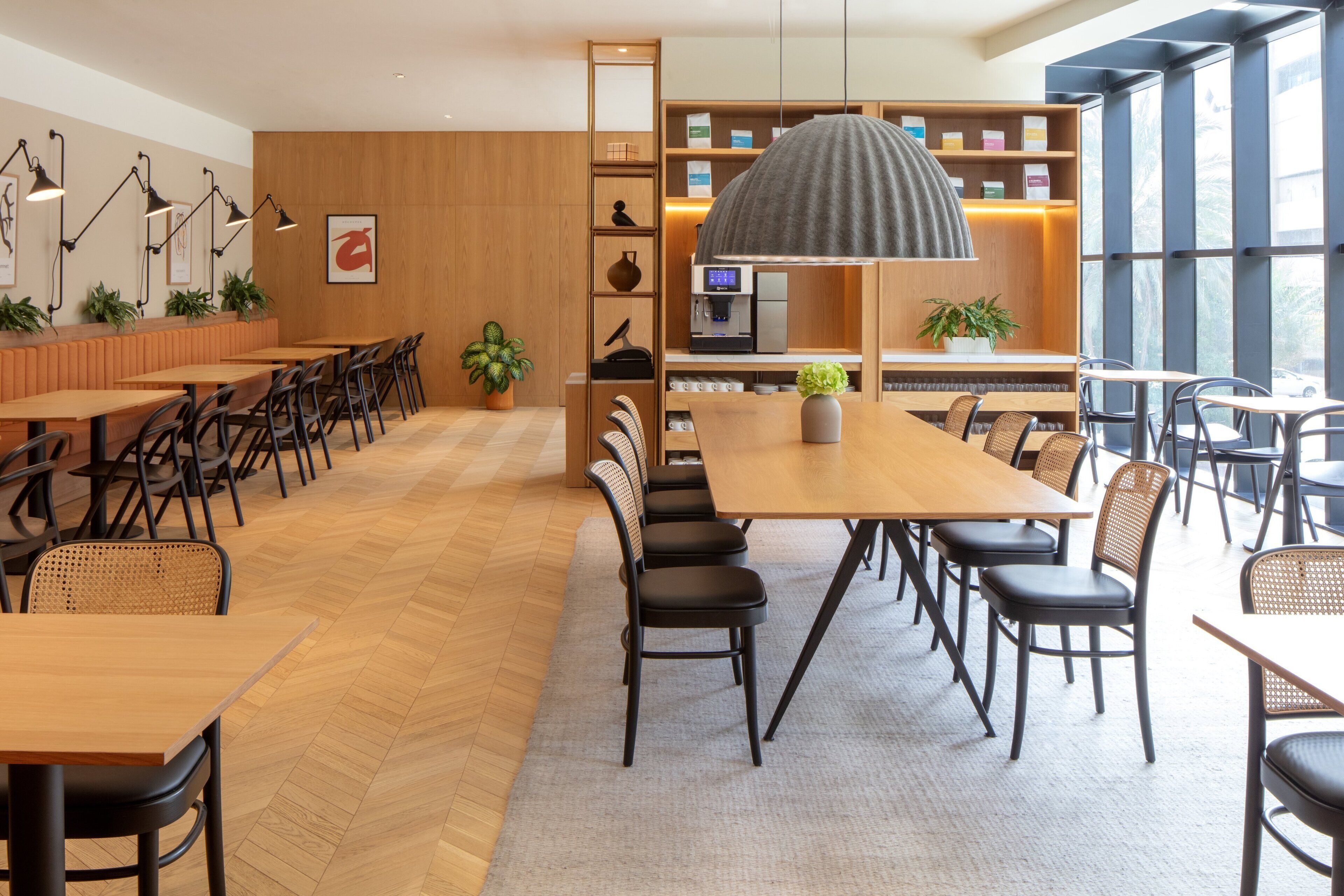 Un café moderne avec des tables et des chaises en bois, un appareil à café et une grande fenêtre laissant entrer la lumière naturelle.