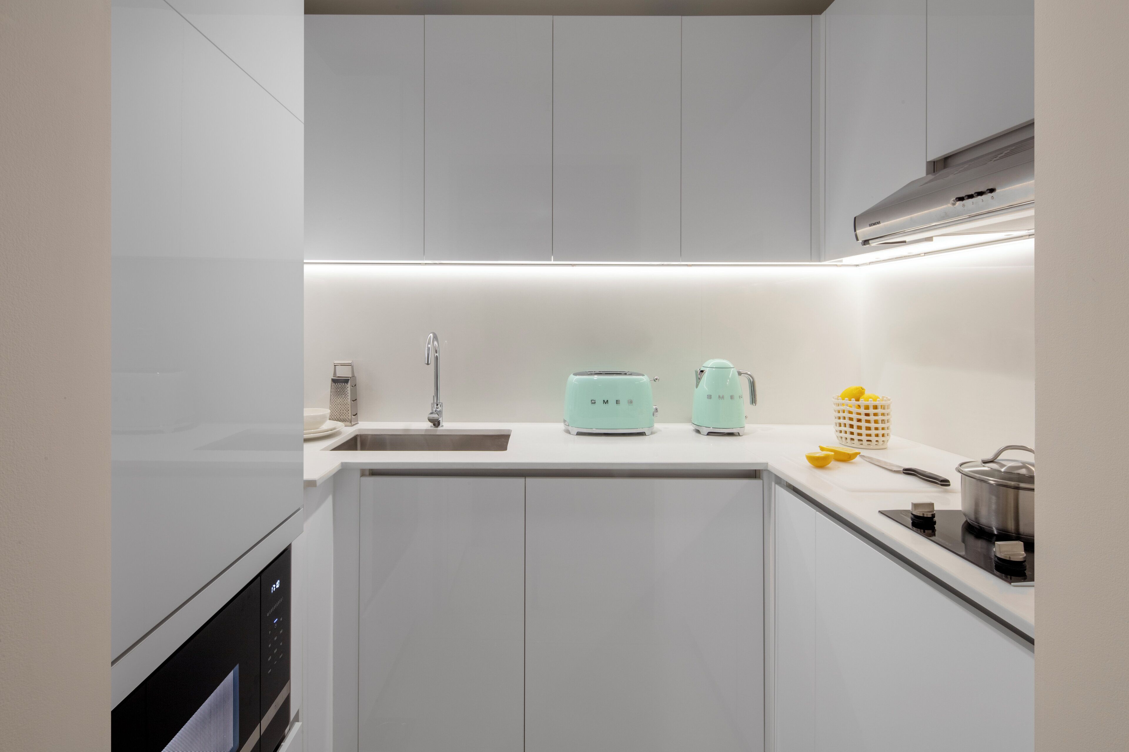 A modern kitchen with white cabinets, a sink, a toaster, and a kettle.