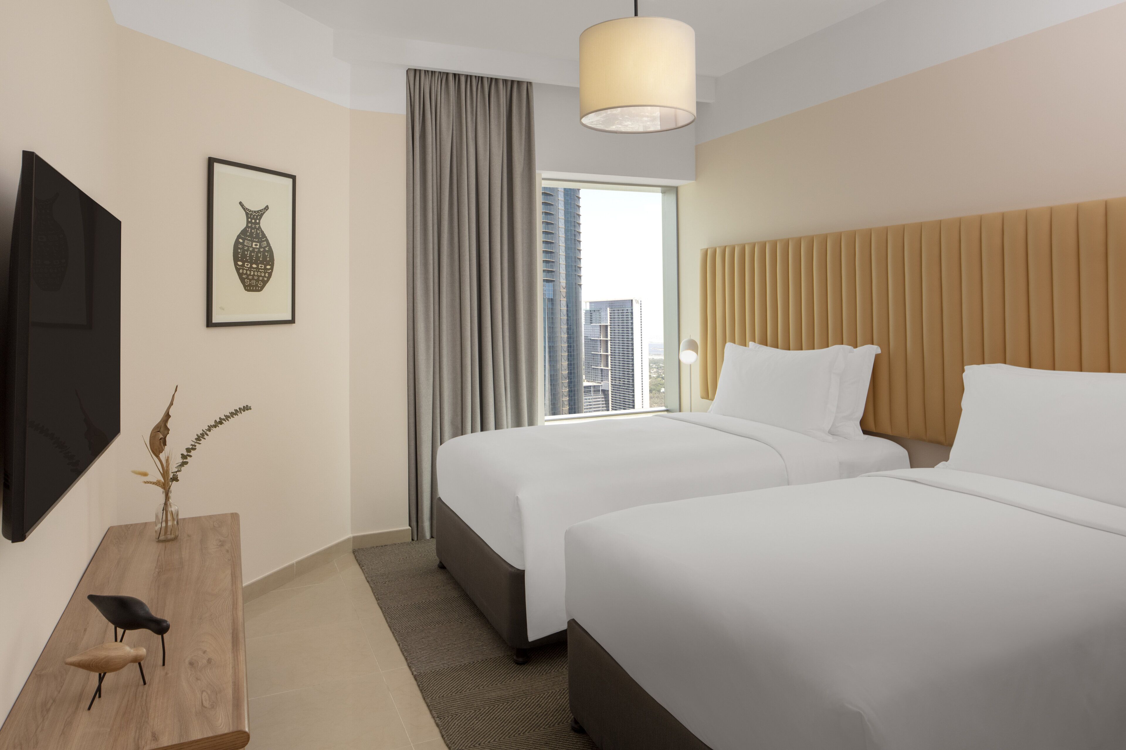 Une chambre d’hôtel avec deux lits, une télévision, un bureau avec des chaises, une fenêtre avec des rideaux et une vue sur la ville.