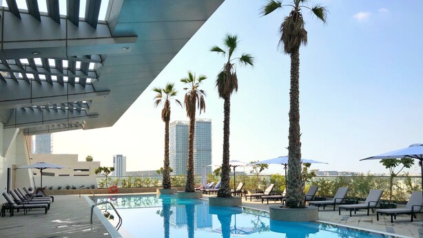 A rooftop pool with lounge chairs and palm trees, surrounded by high-rise buildings. - Staybridge Suites Dubai Financial Centre by IHG (Dubai)