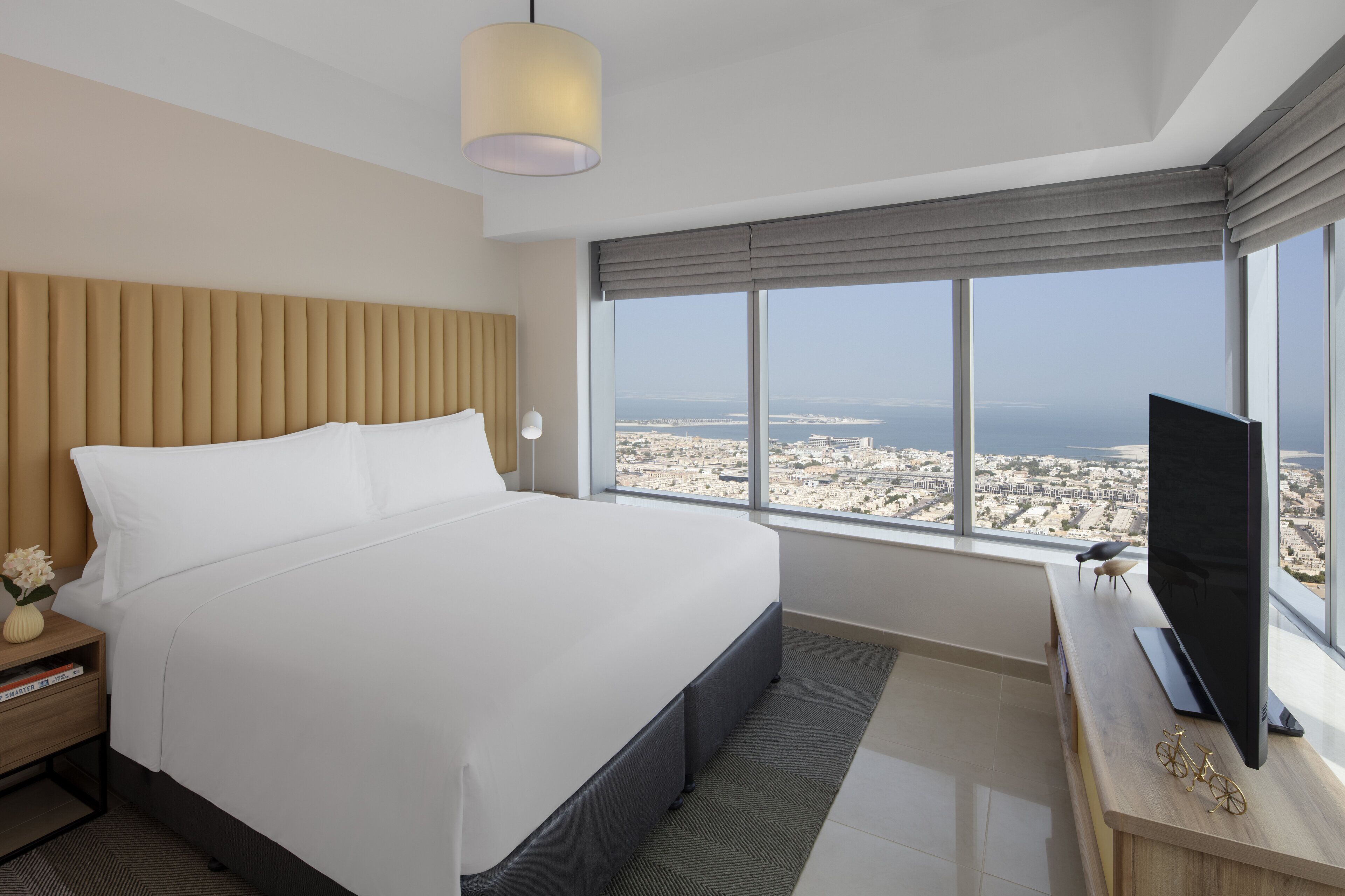 Een moderne hotelkamer met een groot bed, een televisie en een stadsgezicht door grote ramen.