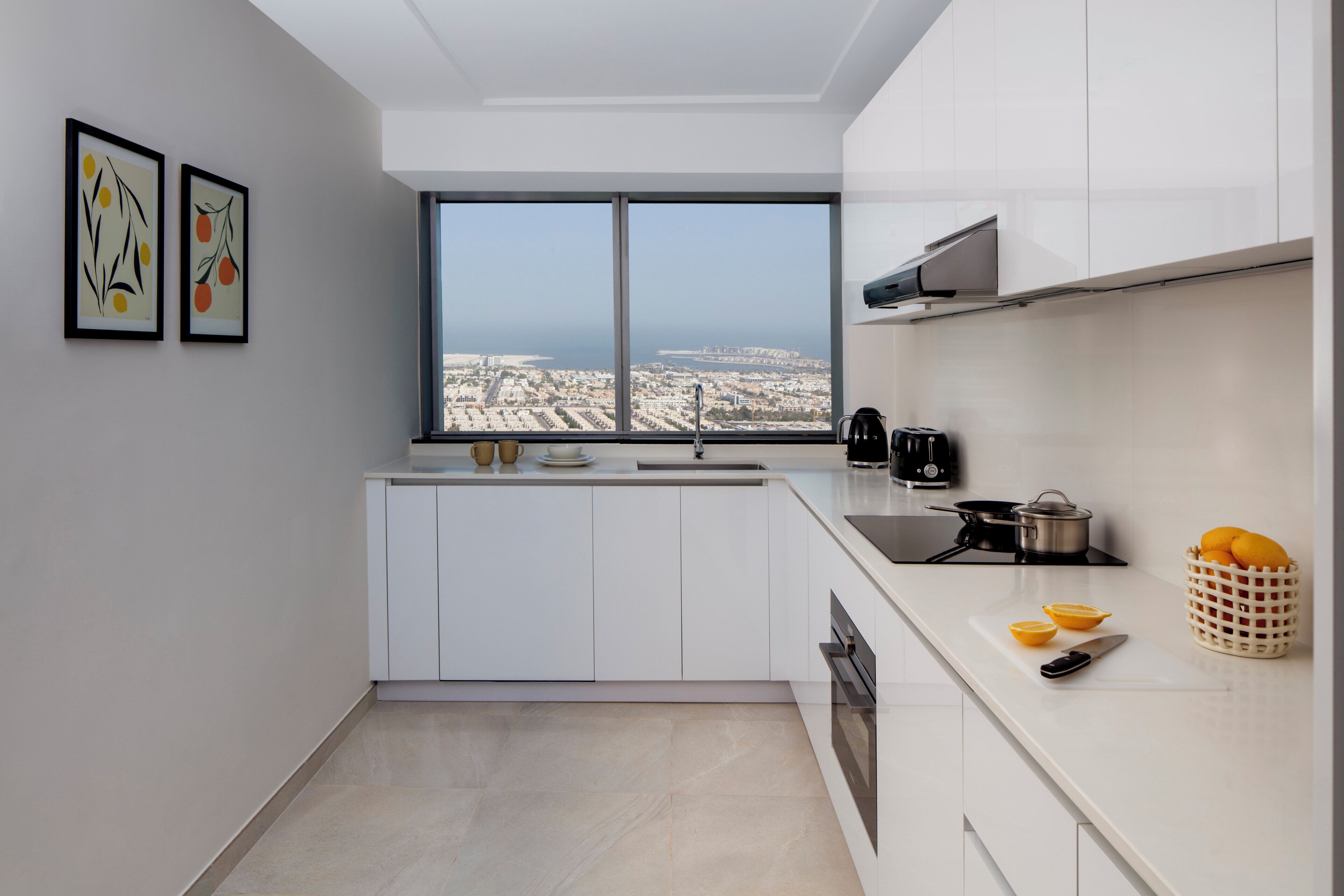 Een moderne keuken met witte kasten, een groot raam met uitzicht op een stadsgezicht en de zee.