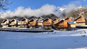 Een rij houten blokhutten met balkons, voor een besneeuwde berg op de achtergrond.