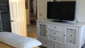 Un dormitorio con cama, cómoda, televisor y puerta que da a otra habitación.