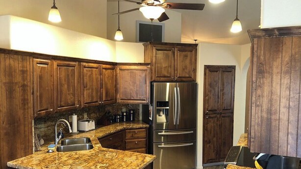 Una cocina con armarios de madera, un refrigerador de acero inoxidable, una encimera de granito y un ventilador de techo.