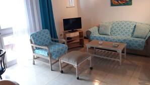 A living room with a sofa, armchair, coffee table, TV, and a painting on the wall. - Town House with full ocean view.   (Negril)