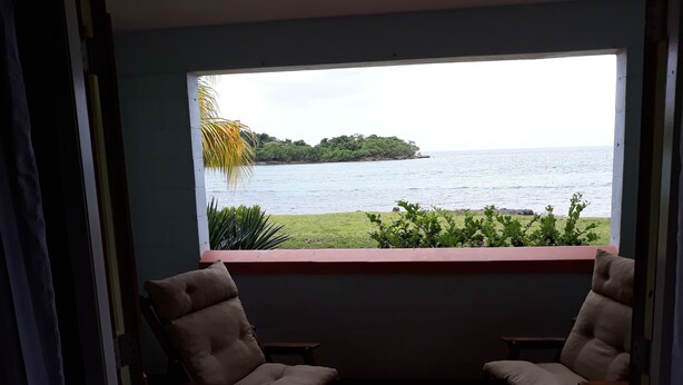 A room with two chairs facing a window overlooking a body of water and a small island. - Town House with full ocean view.   (Negril)