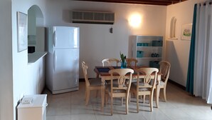A dining area with a white refrigerator, wooden chairs, a table, and a white cabinet with shelves. - Town House with full ocean view.   (Negril)