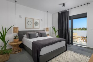 Ein modernes Schlafzimmer mit einem großen Bett, zwei Nachttischen mit Pflanzen, Blick ins Freie durch eine Schiebetür und einem Bild an der Wand.