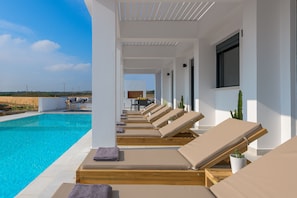 Un espace aménagé au bord de la piscine, avec des chaises longues, une piscine à l’eau cristalline et une vue sur le paysage.
