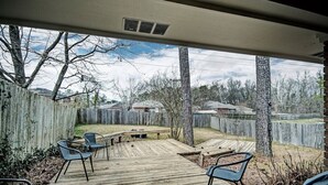 Un patio exterior techado con piso de madera, sillas de metal y una mesa.