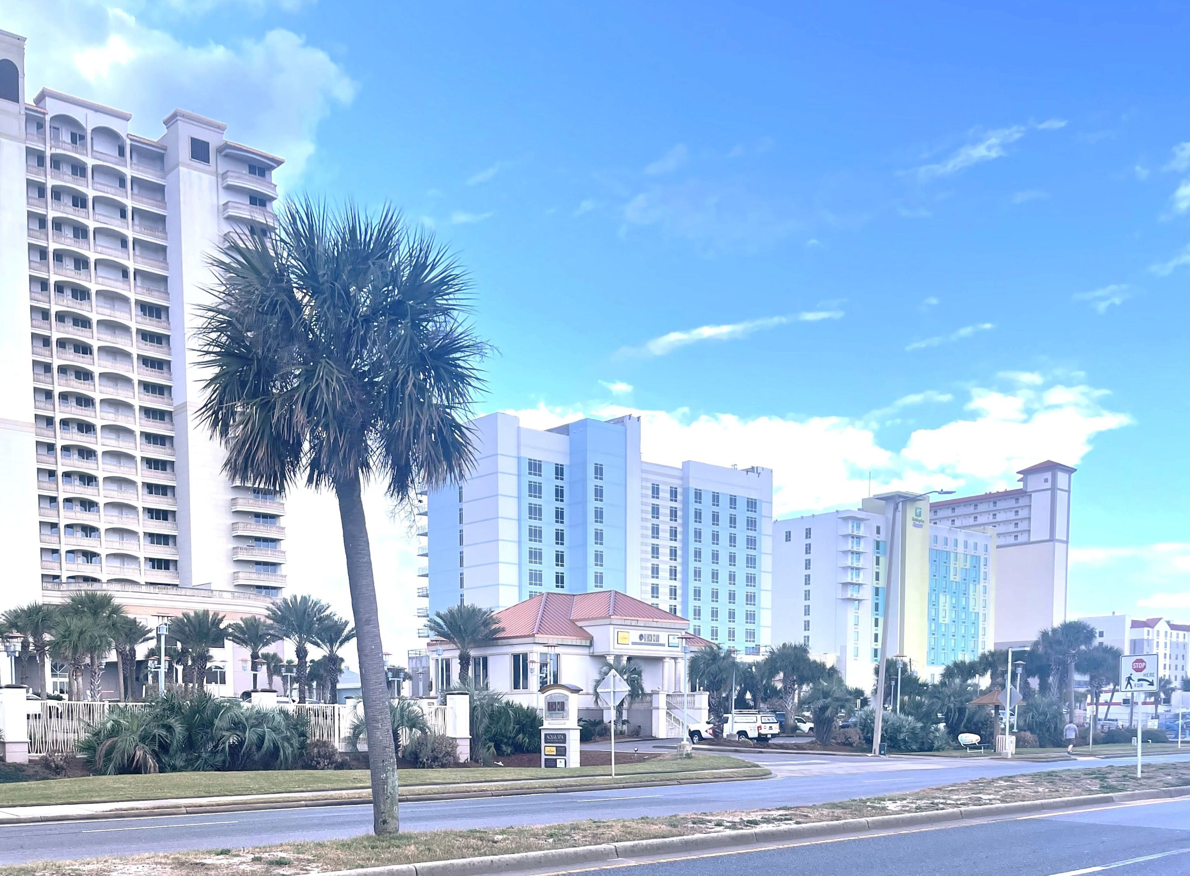 Un hotel de varios pisos, una palmera en primer plano y un cielo azul despejado.