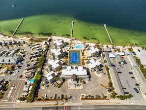 An aerial view of a coastal resort with a central tennis court, multiple buildings, and a marina. - Soundside Holiday Beach Resort (Pensacola Beach)