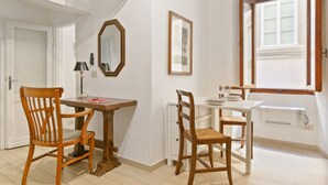 Een kamer met twee houten stoelen, een klein wit tafeltje, een spiegel en een raam met houten kozijnen.