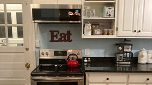 Une cuisine avec des meubles blancs, une cuisinière en acier inoxydable, une bouilloire rouge et un panneau mural sur lequel on peut lire « Mangez ».