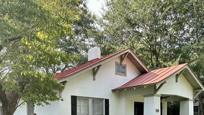Une maison de plain-pied avec un toit rouge, des murs extérieurs blancs et un porche à l’avant.