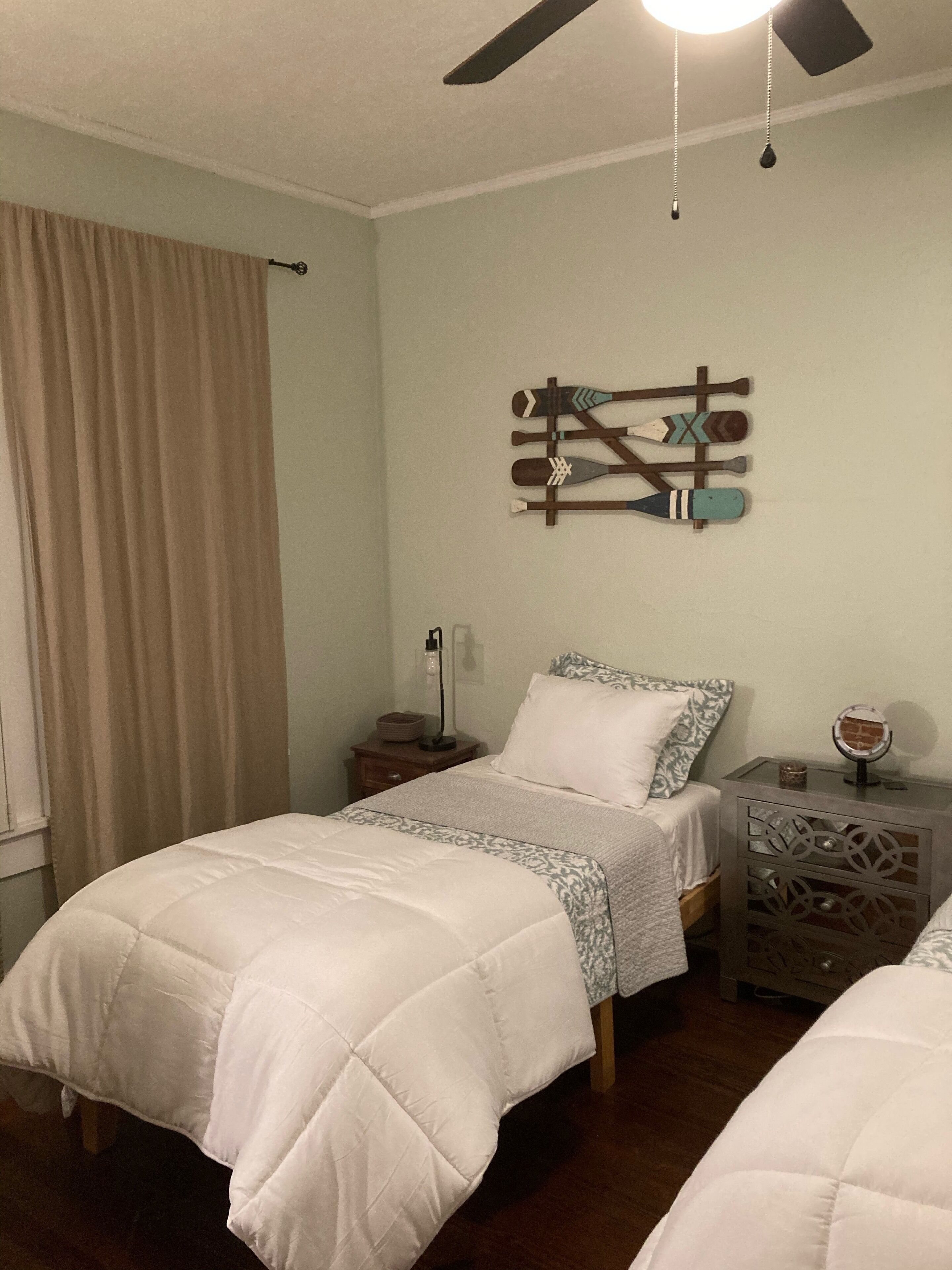 A bedroom with a bed, a nightstand, a dresser, a ceiling fan, and a wall-mounted decoration.