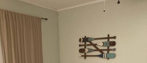 A bedroom with a bed, a nightstand, a dresser, a ceiling fan, and a wall-mounted decoration.