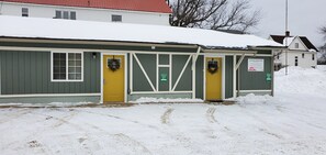 Ein kleines, eingeschossiges Gebäude mit grüner Fassade und gelben Türen, mit einem Schild für eine Immobilienagentur.