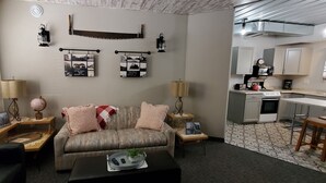 Uma sala de estar com sofá, mesa de centro e uma área de cozinha com armários e fogão.