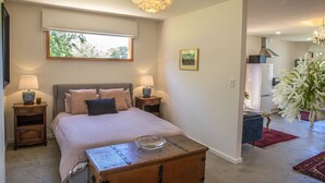 A bedroom with a large bed, bedside tables, a wooden nightstand, a chandelier, a window, and a view into the kitchen. - Seaside Retreat - Premium Luxe Accommodation: 3rd night complimentary: winter 26 (Port Elliot)