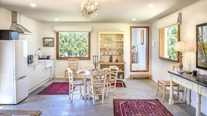 A kitchen with a dining area, wooden chairs, a chandelier, and a window with a view of greenery. - Seaside Retreat - Premium Luxe Accommodation: 3rd night complimentary: winter 26 (Port Elliot)