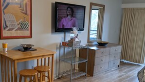 A living room with a wooden dining table, two bar stools, a TV mounted on the wall, a metal shelf unit, and a wooden cabinet. - Hidden gem in the heart of Ocean Creek (Myrtle Beach)