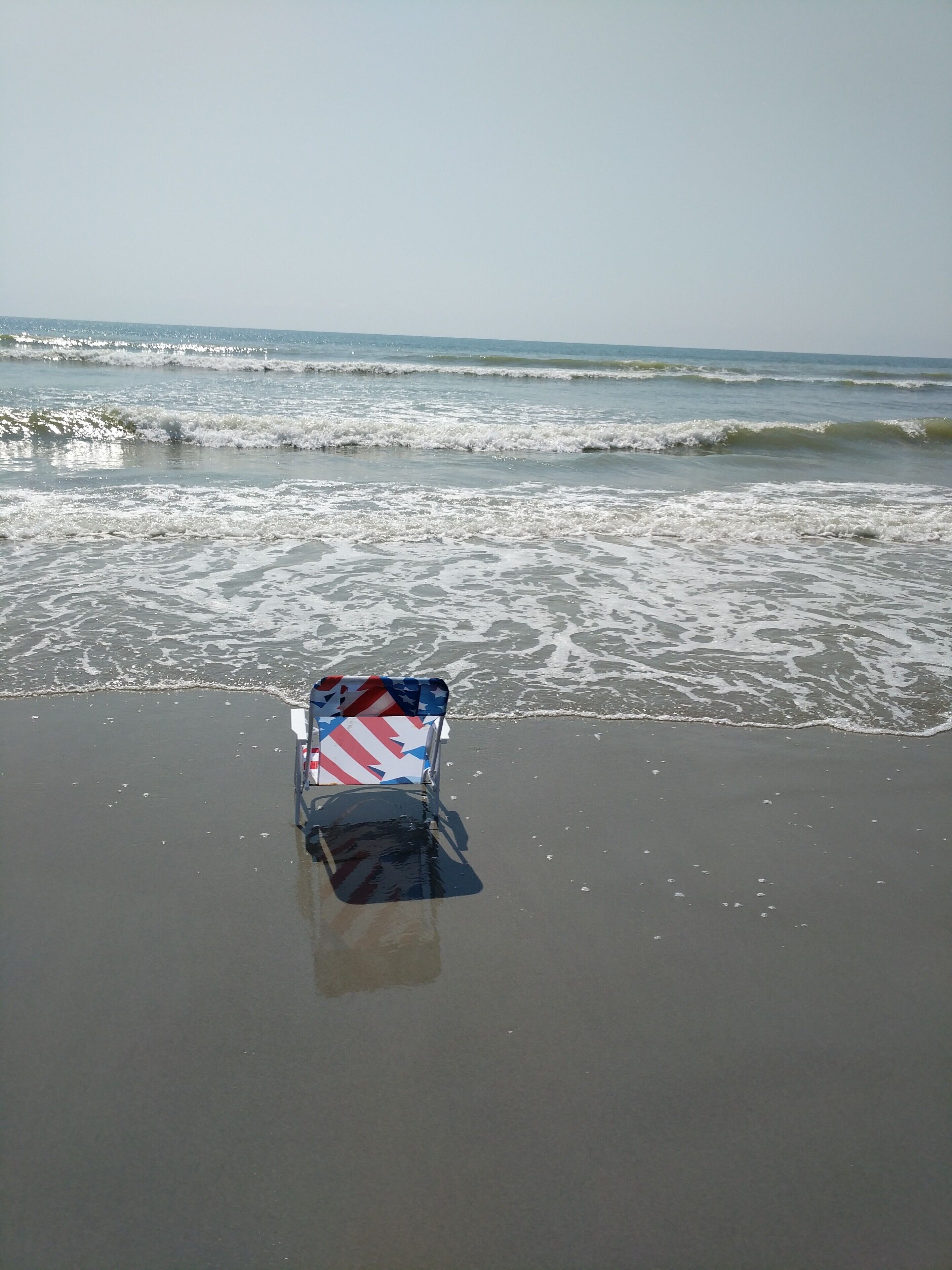 A beach scene with a beach chair and umbrella.