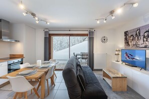 A modern living room with a sofa, dining table, and chairs, a television, and a large window with a view of a snowy landscape.