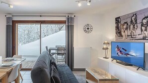 Un soggiorno moderno con un divano, un tavolo da pranzo con sedie, una televisione e una grande finestra che si affaccia su un paesaggio innevato.