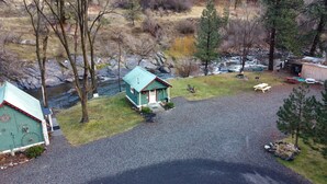 Eine kleine Holzhütte mit einem grünen Dach, einer Schotterauffahrt und einem Fluss im Hintergrund.