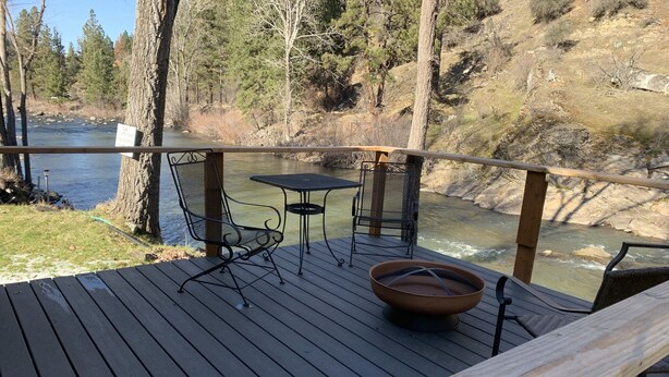 Eine Holzterrasse mit einem Metalltisch und -stühlen mit Blick auf einen Fluss.