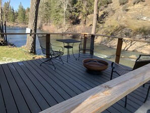 Une terrasse en bois avec une table et des chaises en métal, donnant sur une rivière.