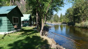 Eine Hütte mit grüner Fassade, einer kleinen Veranda und einem Fluss im Hintergrund.