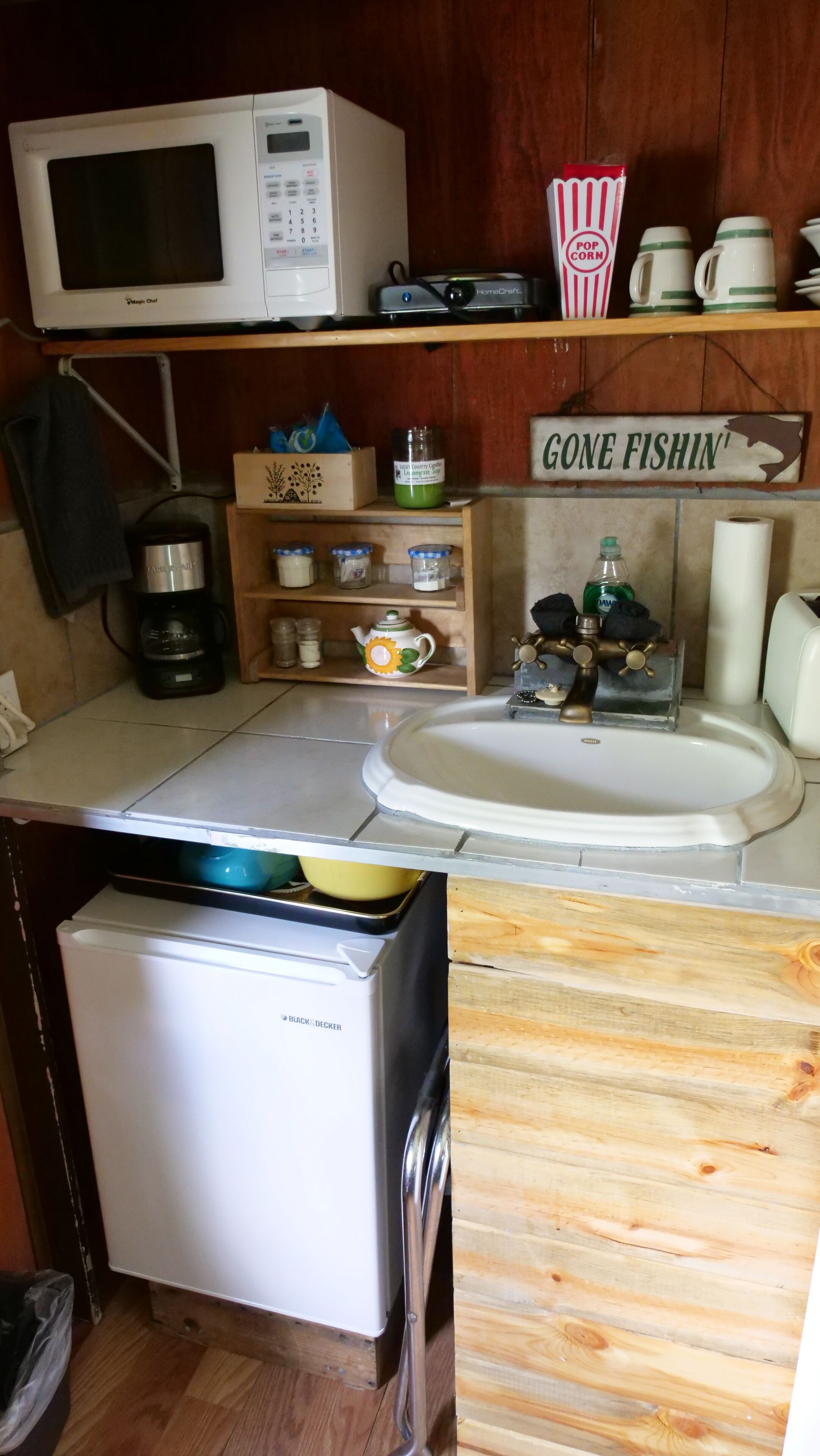 A compact kitchen with a microwave, coffee maker, and a sink. There are wooden cabinets and a small refrigerator.
