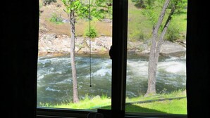 Blick aus dem Fenster auf einen Fluss, mit einem Baum im Vordergrund und einer felsigen Landschaft im Hintergrund.
