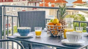 Een balkon met een ontbijttafel, inclusief een schaal fruit, glazen sinaasappelsap en een ananas.