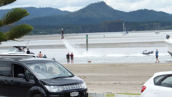 A beach with a water jet ski activity, a boat, and a car parked on the sand.