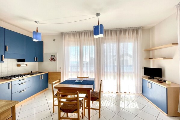 A modern kitchen with blue cabinets, a dining table, and a TV on a wooden cabinet.