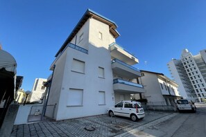 A multi-story residential building with balconies and a car parked in front.