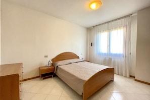 Un dormitorio con una cama de madera, una mesita de noche, un escritorio y una ventana con cortinas.