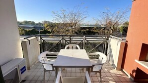 Un balcon avec une table et des chaises, une vue sur des arbres et un pont, et un bâtiment en arrière-plan.