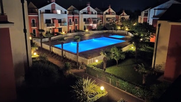 Une piscine entourée de bâtiments dotés de balcons, de chemins bien éclairés et de jardins aménagés.