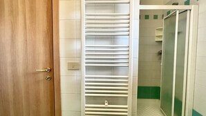 Une salle de bain avec une porte en bois, un porte-serviettes blanc et un espace douche aux carreaux verts.