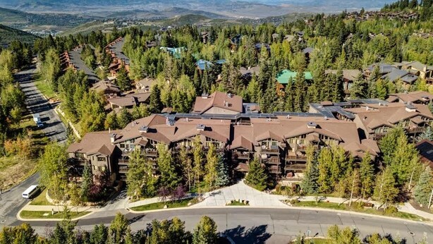 A resort with multiple buildings surrounded by trees, a central road, and a view of distant mountains.