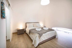 A bedroom with a bed, bedside tables, a nightstand, a hanging artwork, and a window.